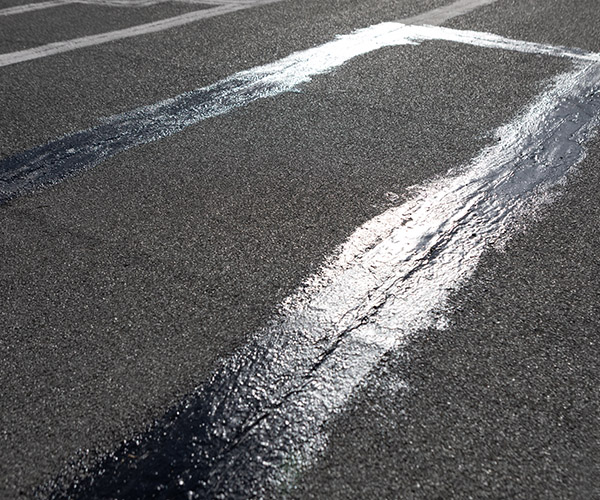 Luting lines stretch across a cracked, roof surface sealed with fresh, reflective tar. Contrast between textures hints at wear and repair, marking a utilitarian space of rooftop